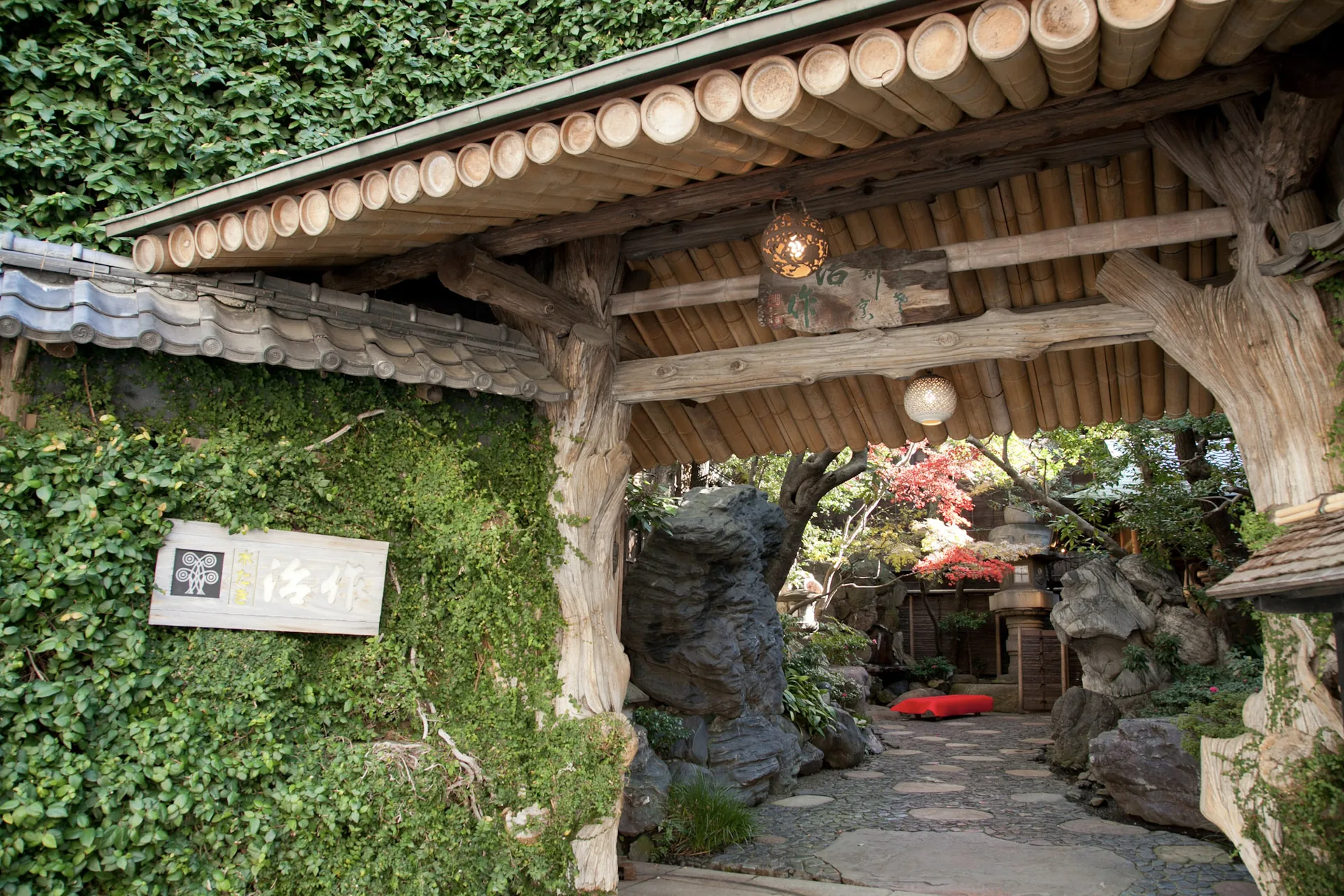 The ivy-covered wooden entrance gate of Tsukiji Jisaku, lit by a hanging lantern