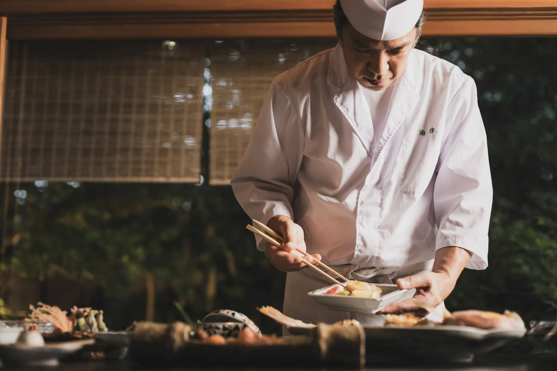 A chef at Tsukiji Jisaku plating a seasonal kaiseki dish with cooking chopsticks