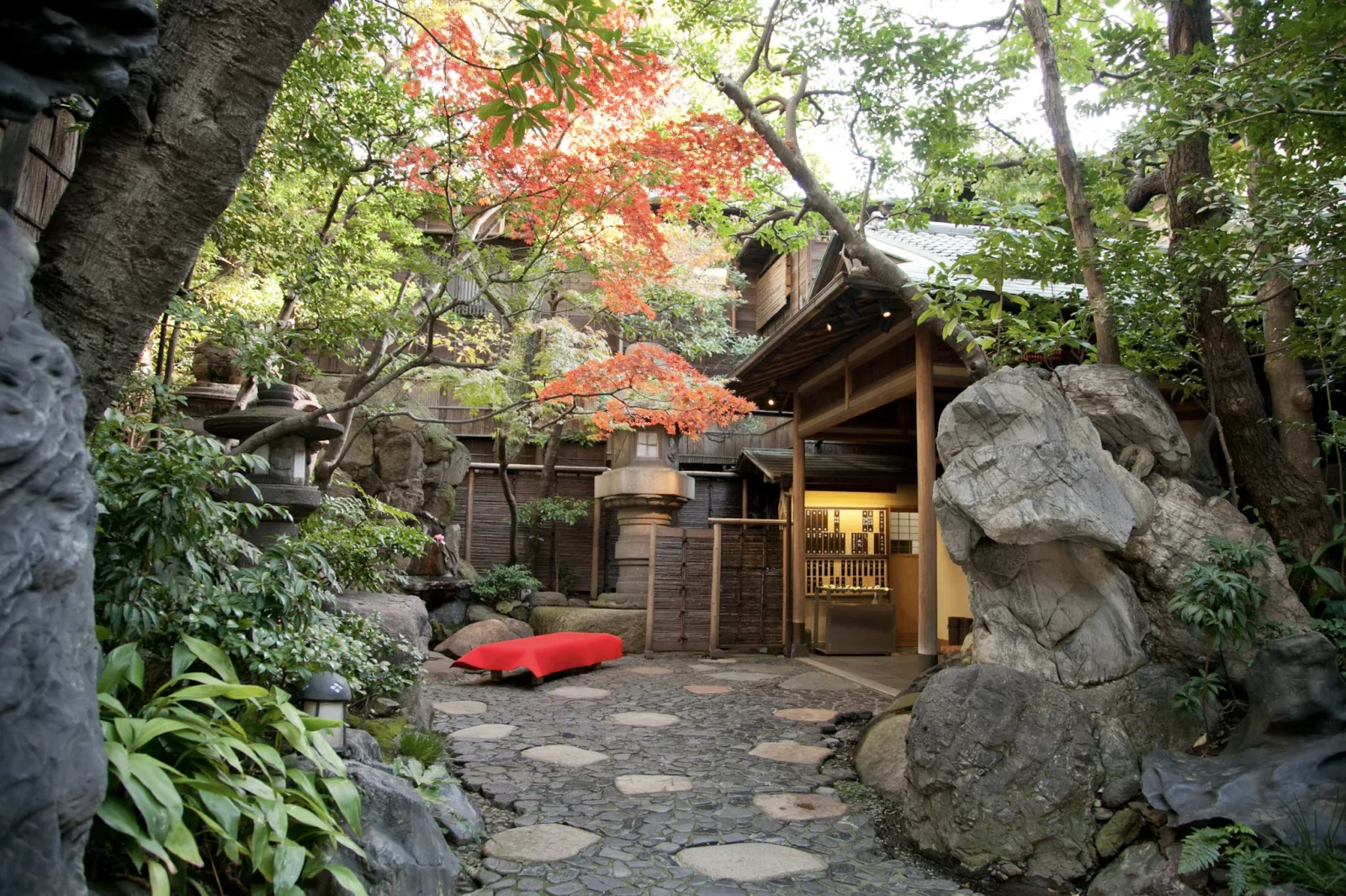 The entrance garden of Tsukiji Jisaku in autumn, maples turning red above the stone path to the door
