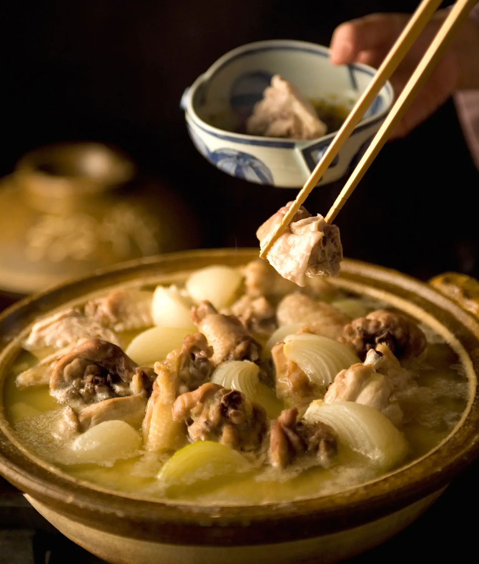 Mizutaki being served from the donabe with cooking chopsticks, the broth clear and golden